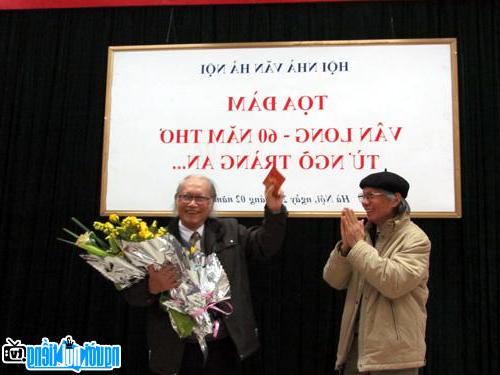 Nhà thơ Vân Long (phải) nhận hoa chúc mừng của nhà văn Hoàng Quốc Hải